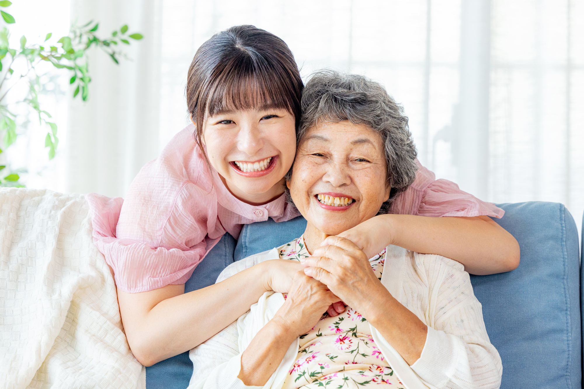 ソファに座る祖母を後ろから抱きしめている笑顔の孫
