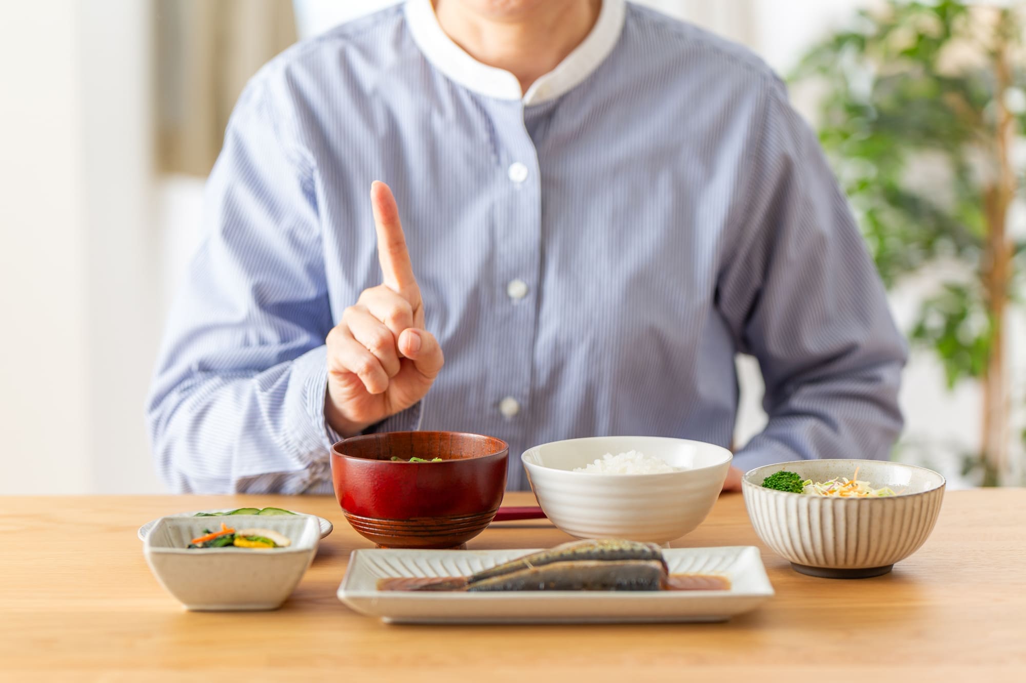 和食を前に人さし指を立てる人物の手元