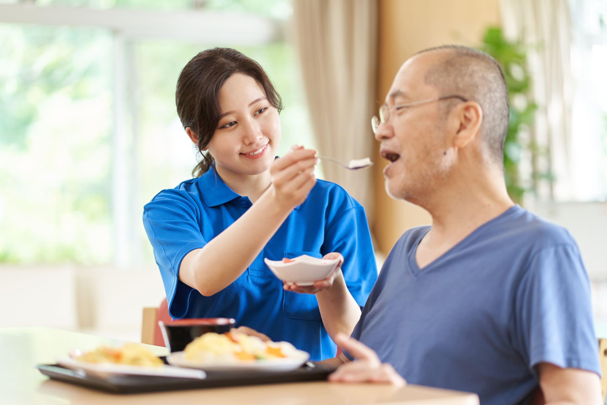 介護食をスプーンで食べさせてもらっているシニア男性