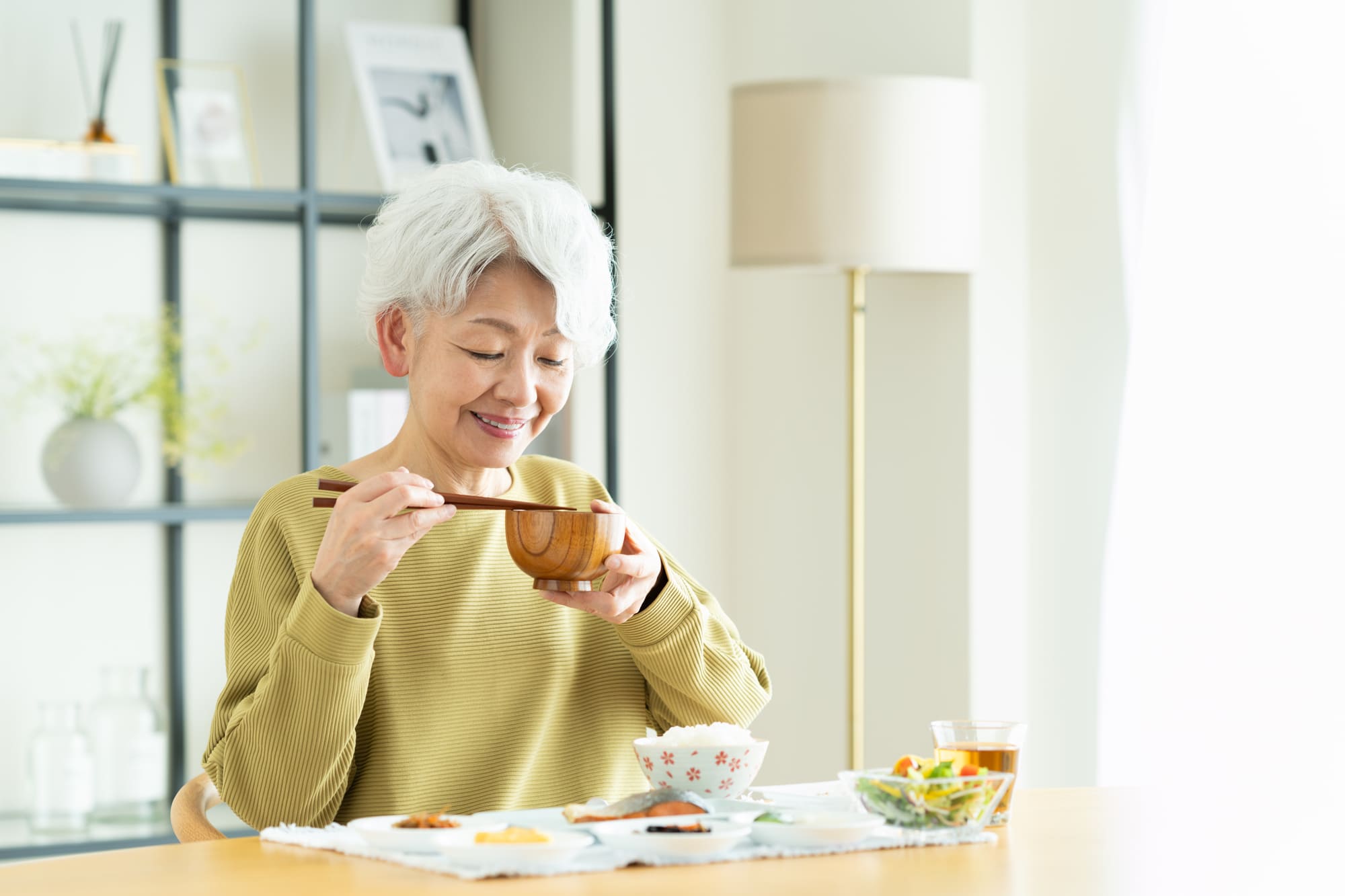 みそ汁のお椀を持ち、食事を楽しむシニア女性