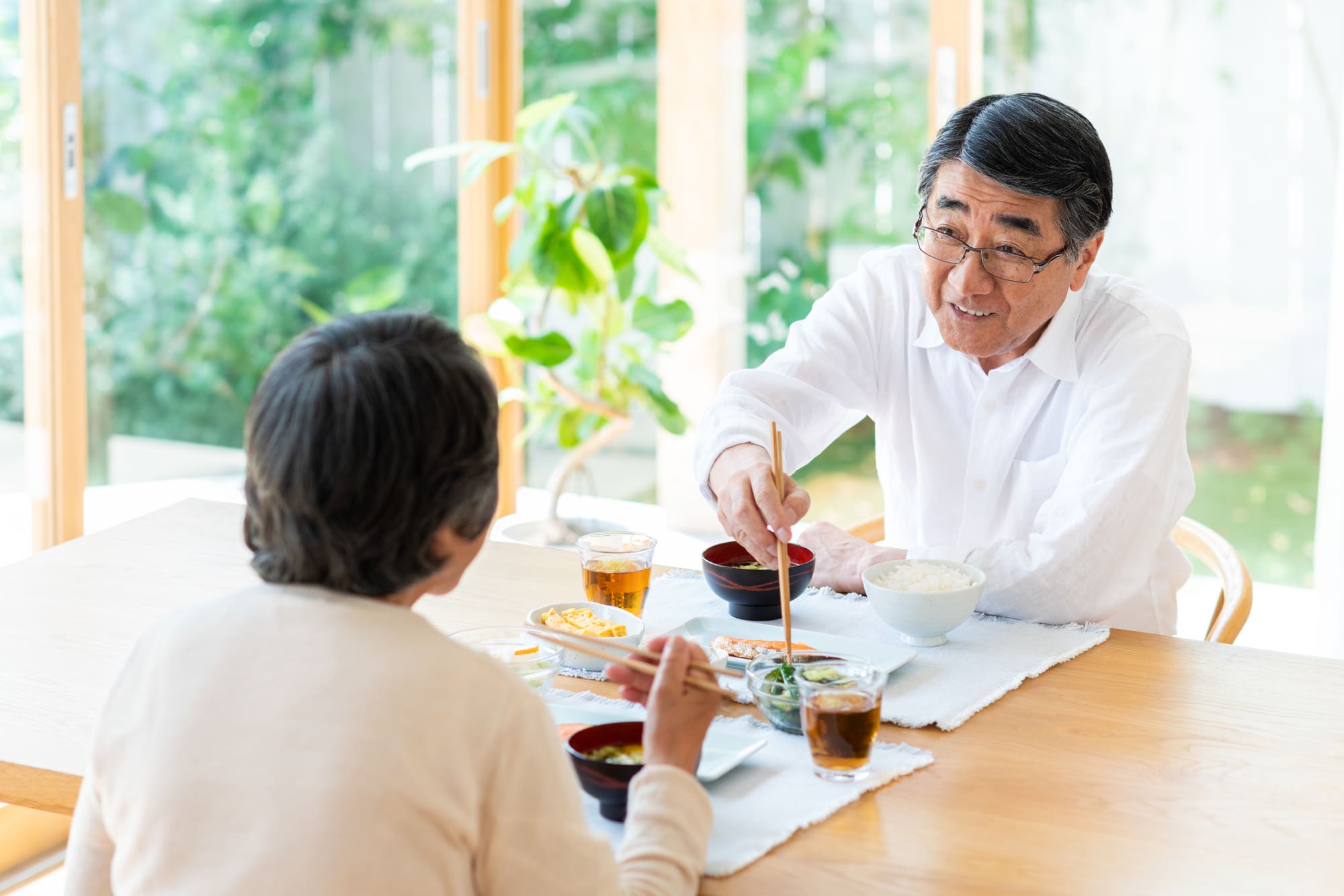 向かい合わせに座り、笑顔で食事を楽しむシニア夫婦