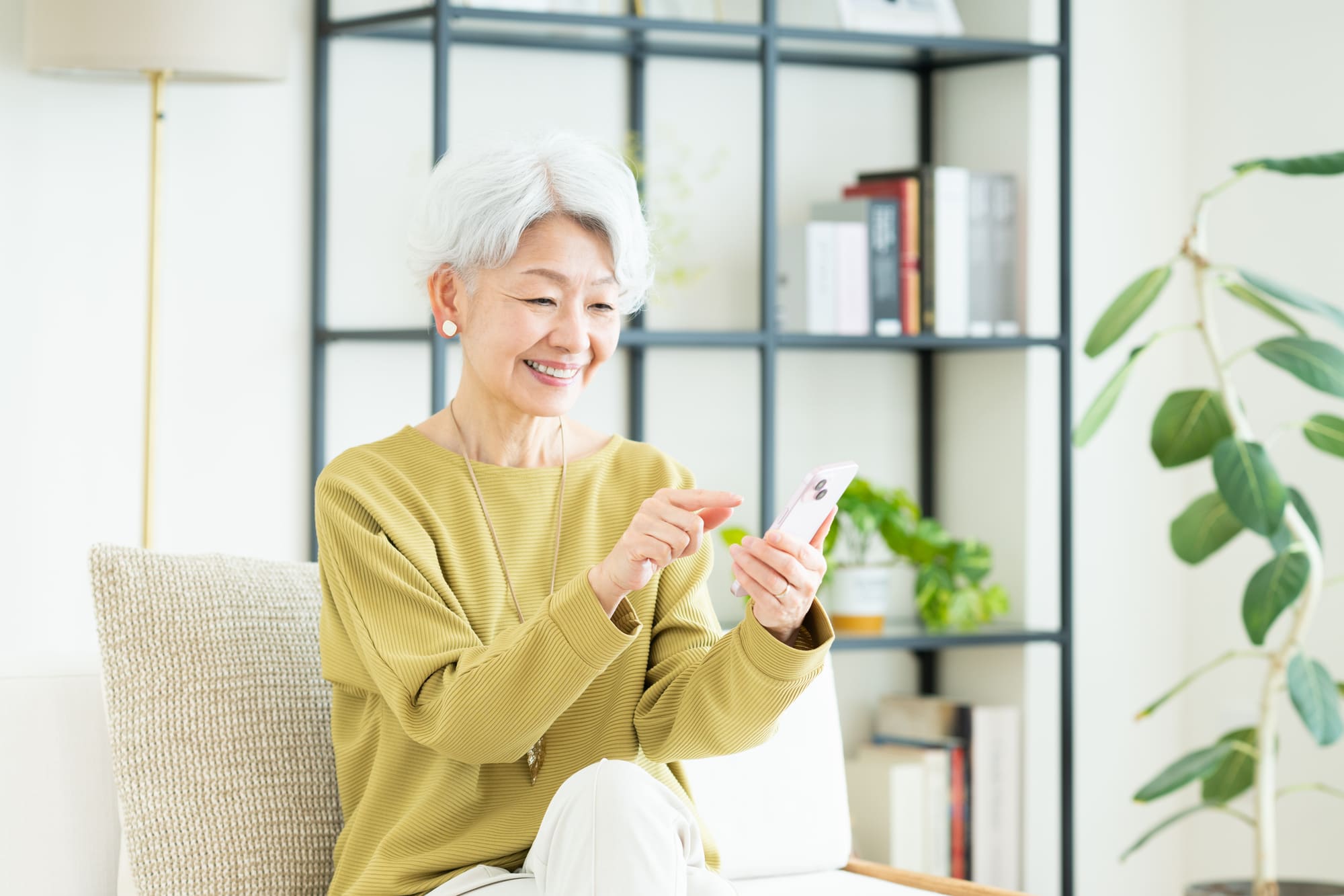 リビングでスマホを操作するシニア女性