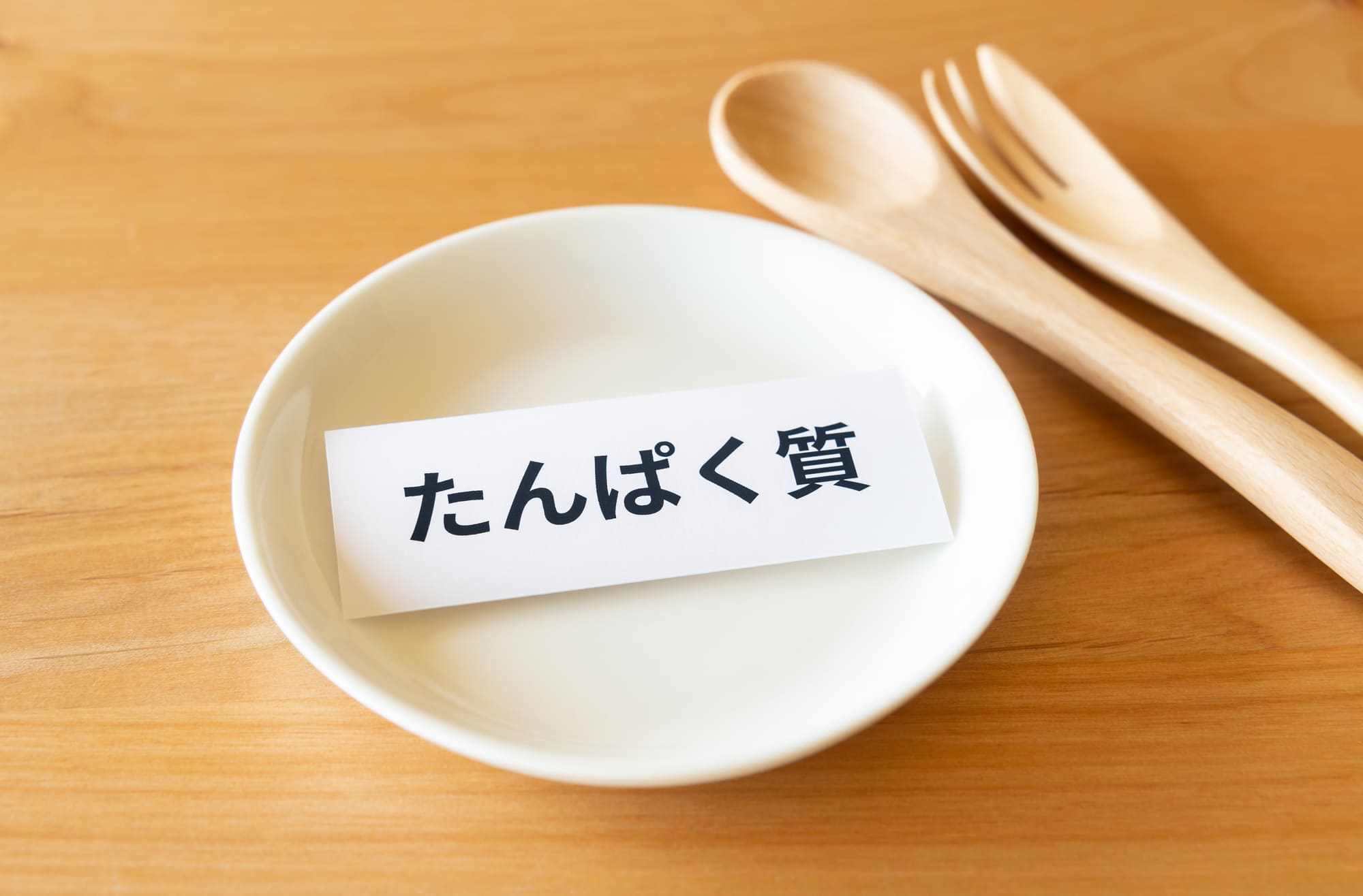 「たんぱく質」を書かれた紙が乗った白い皿と木のカトラリー
