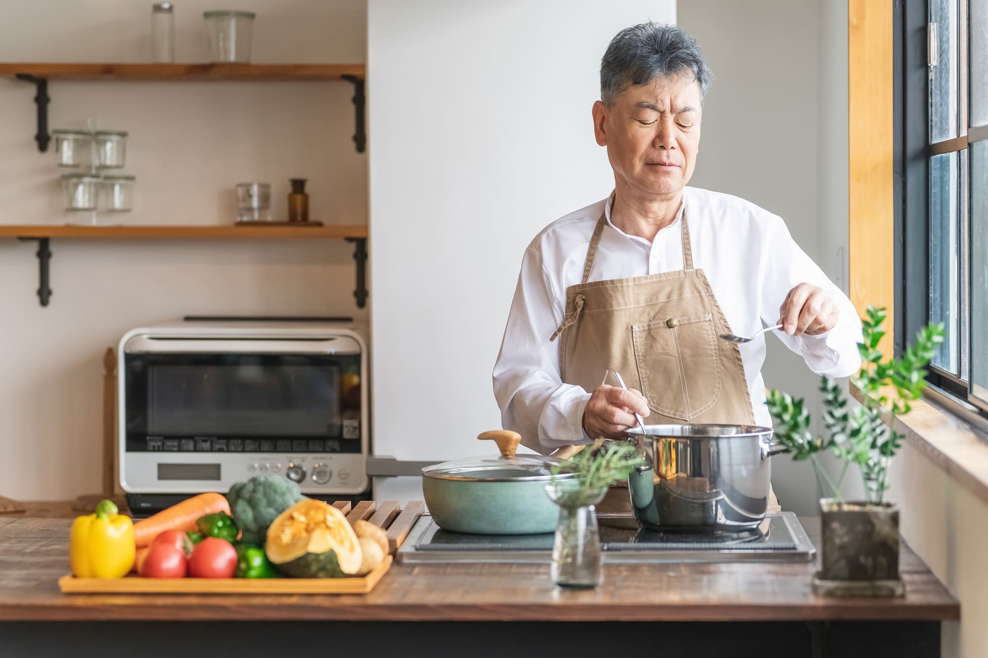 キッチンで悩みながら料理をするシニア男性