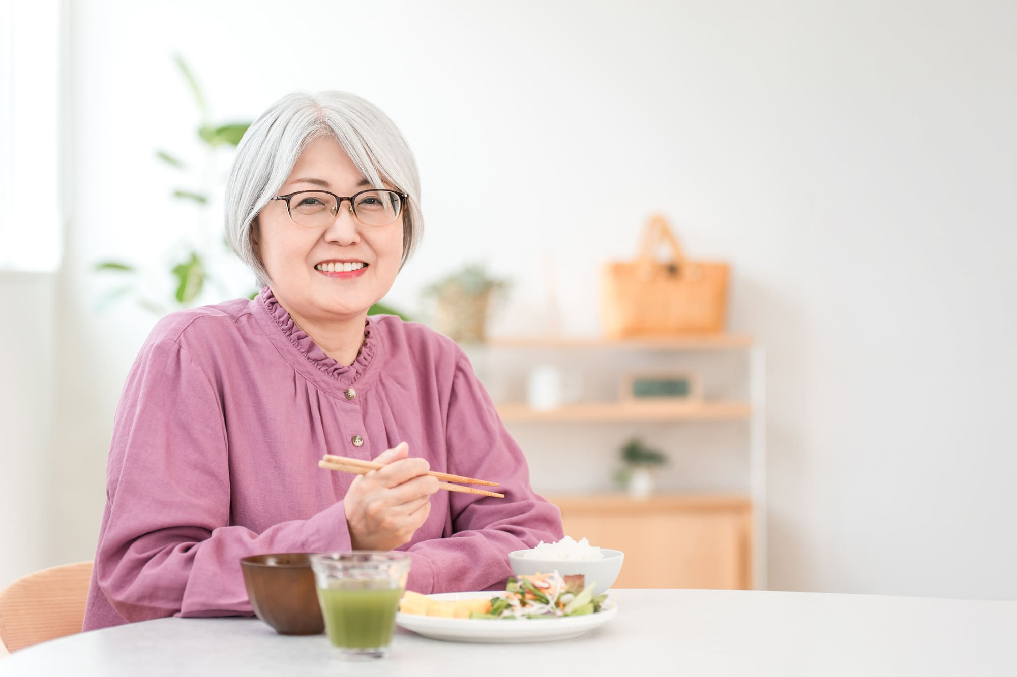 食事が用意されたテーブルと椅子に座る笑顔のシニア女性