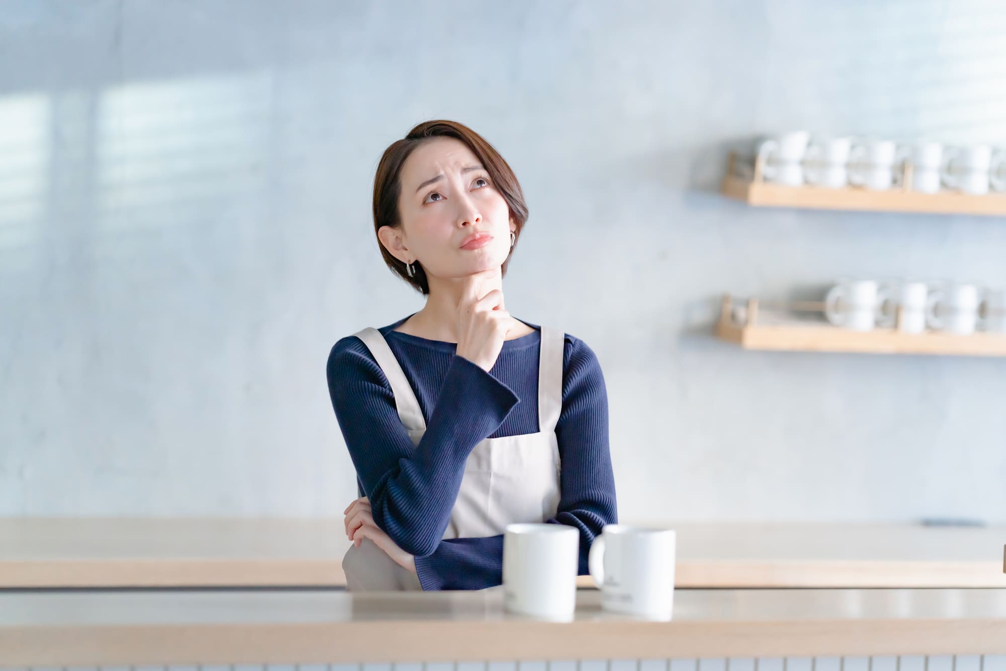 顎に手を当てて、キッチンで考える女性
