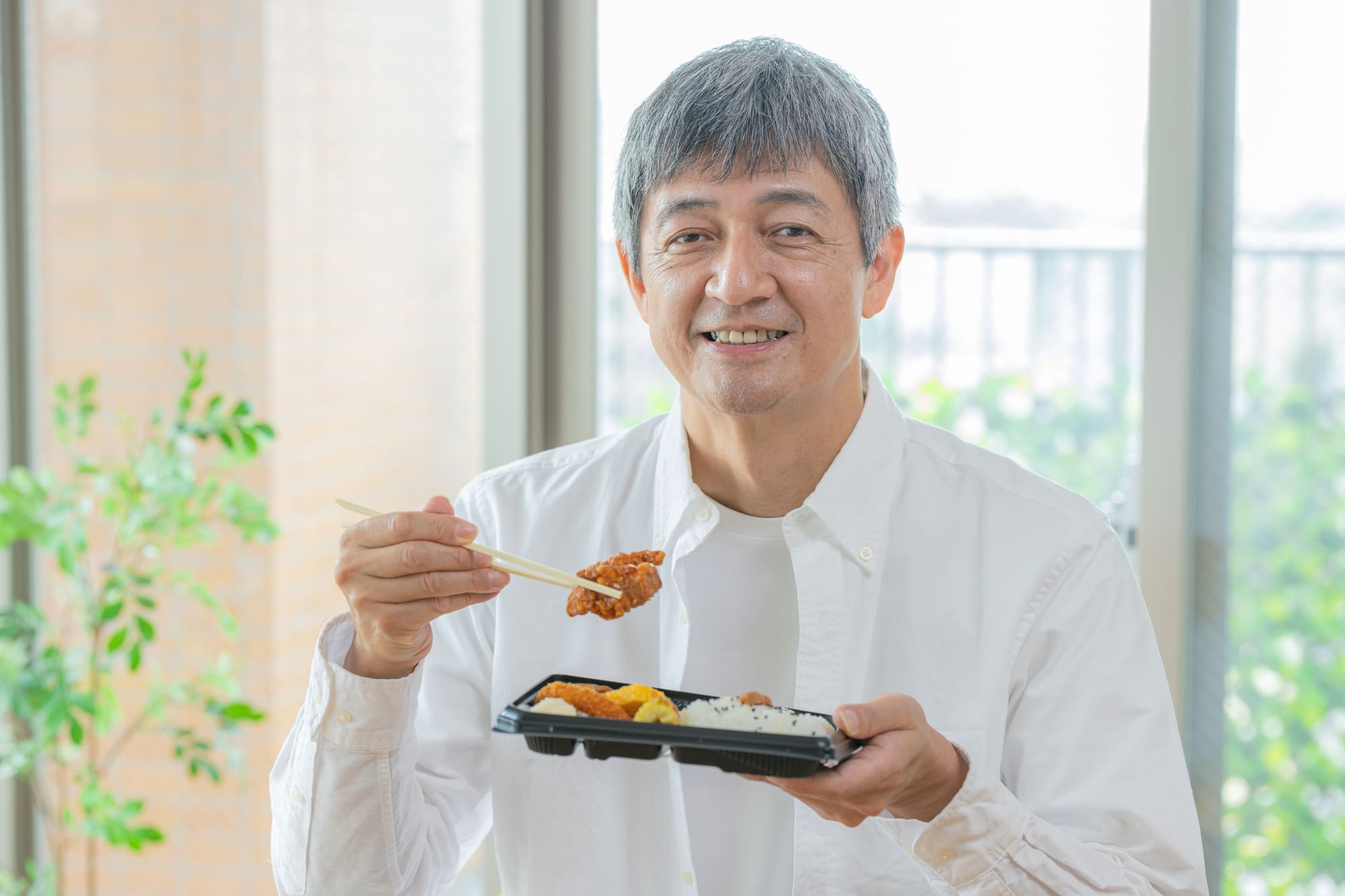 弁当を手に持って食べようとしているシニア男性