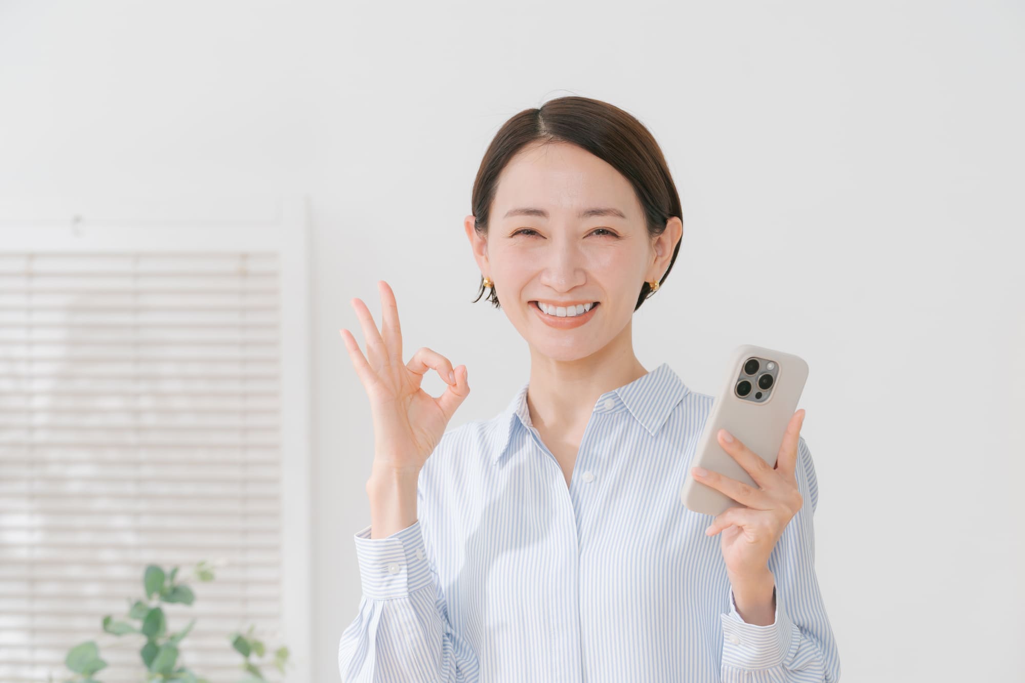 スマホを持ち、指でOKマークを作る笑顔のミドル女性