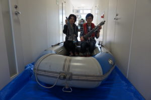 こちらは環境地球化学研究室のブースです。この研究室では、水や森林、大気など地球規模で環境の変動・変化を研究しています。今回は先生や学生が調査の際に実際に使用しているボートを展示。参加者の方に乗っていただきました。手に持っているのは深いところの水を採取する機械。溺れないようにライフジャケットも着用していただきました!