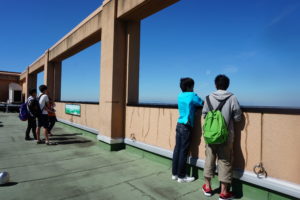 オープンキャンパスが終了する15時半ギリギリまで、学生スタッフが同行する学内キャンパスツアーも行っておりました。今皆さんがいるのは本学で1番背の高い建物、中央館の屋上です。屋上には本学に入学してしまうと入れなくなるので、オープンキャンパスに参加してくれた方だけの特権です!ちなみにどんな景色なのかと言うと…