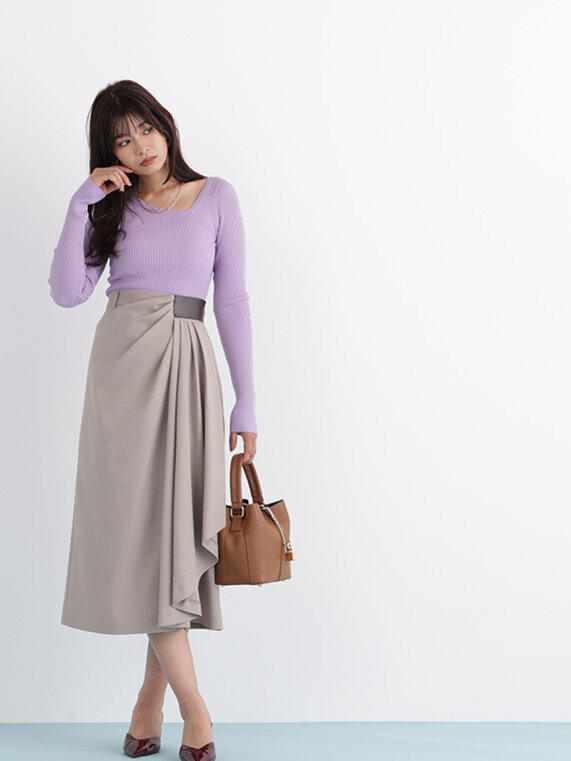パープルのアシメネックニットプルオーバーにベージュのスカート。ブラウンのバッグ。