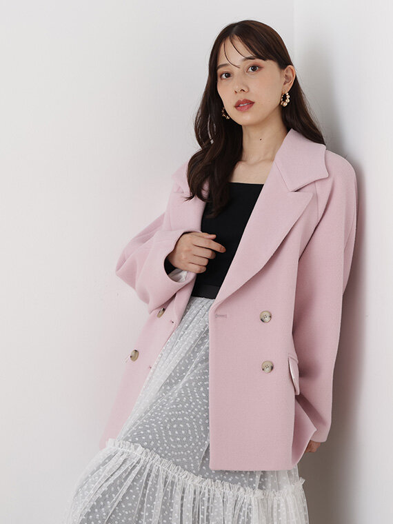 ベイビーピンクのコートにブラックのニットプルオーバー、ホワイトのロングスカートのコーディネート