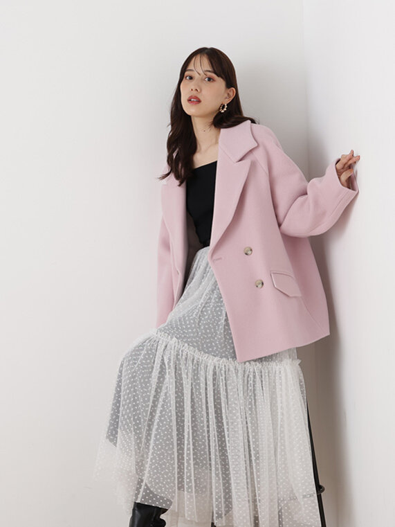 ベイビーピンクのコートにブラックのニットプルオーバー、ホワイトのロングスカートのコーディネート