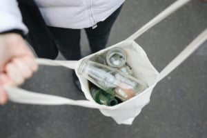 Person holds a canvas bag filled with glass jars and bottles for recycling