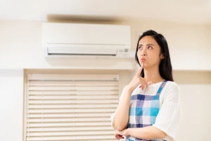 エアコンの前で悩む女性の写真