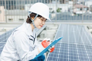 太陽光パネルの横で何かをメモする専門修理事業者の写真