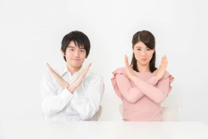 手でバツ印を作る男女の写真