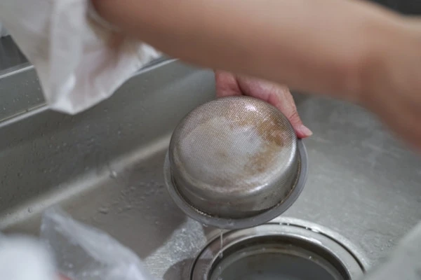 キッチンの排水溝の流れが悪くなるのを防ぐためにゴミ受けを掃除する様子