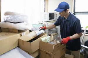 散らかった部屋の片付けをする男性作業員の写真