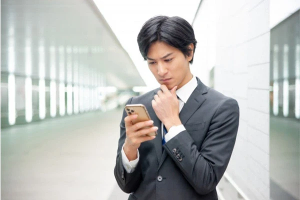 スマートフォンを見ながら悩んでいるスーツの男性