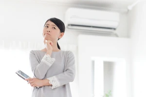 エアコンの前で悩んでいる女性の写真