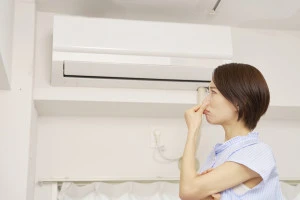 エアコンの臭いに困る女性の写真