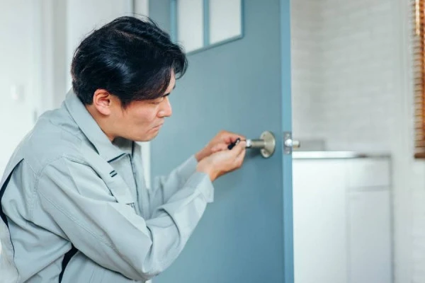 作業服の鍵屋がドアの鍵を修理する様子