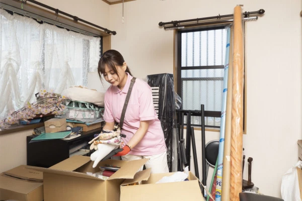散らかった部屋の片付けをする女性作業員の写真