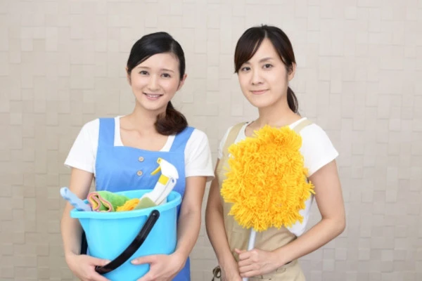 掃除道具を抱え笑顔で微笑む女性の様子