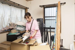 散らかった部屋の片付けをする女性作業員の写真