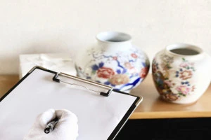 2つの壺と箱を査定するクリップボードと白手袋の手元の写真