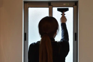 窓にフィルムを貼る女性の写真