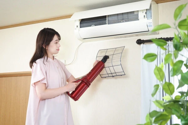 エアコンのフィルターを掃除機で掃除する女性