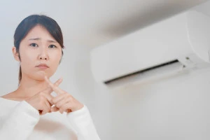 エアコンの前で指でバツ印を作る女性の写真