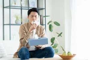 家の中で花粉症に苦しむ男性の写真