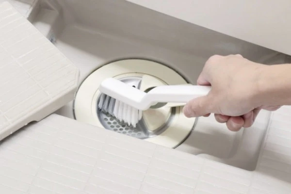 お風呂の排水溝に水がたまらないようにブラシで掃除する様子
