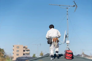 屋根に登ってアンテナ工事を行う作業員の写真
