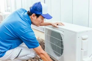 エアコンの室外機と作業着の男性の写真