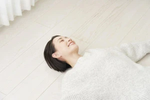 フローリングに仰向けで寝転ぶ女性の写真