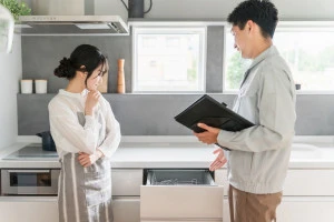 キッチンで水道屋・設備屋に食洗機・食器洗浄器の説明を受ける主婦の女性の写真