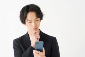 スマホを片手に考える男性の写真