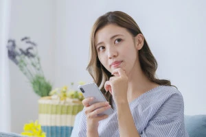 スマホを片手に考える女性の写真