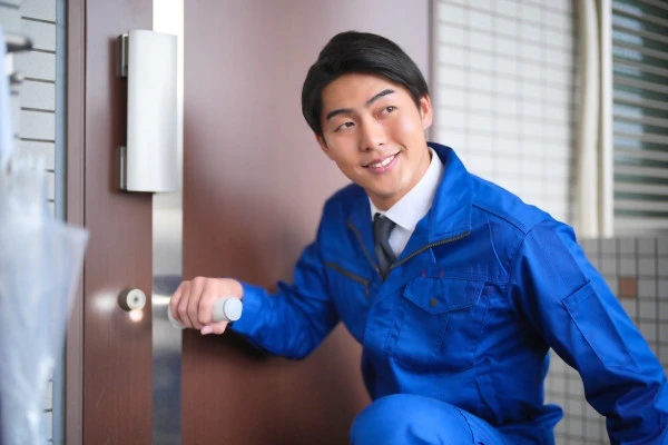 作業着姿の男性が笑顔で玄関ドアの作業をしている写真