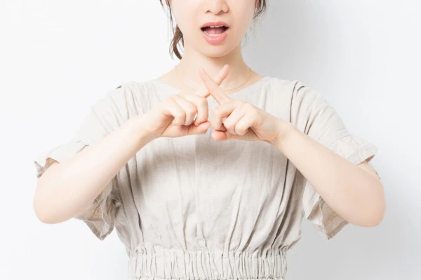 白背景の前に立って、NGのジェスチャーをする女性の写真