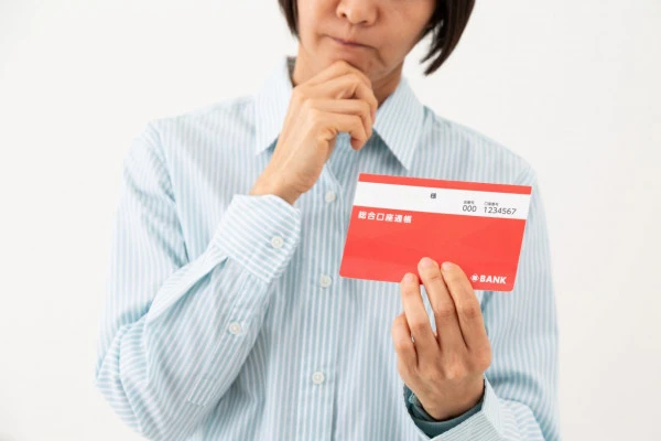 預金通帳を持って悩むミドル女性の写真