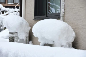 雪に埋もれた室外機の写真