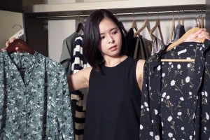 似たような服を両手に持って悩む女性の写真