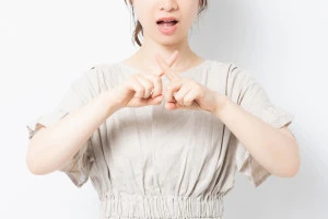 白背景の前に立って、NGのジェスチャーをする女性の写真