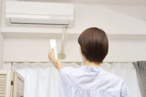 エアコンの電源を入れようとしている女性の写真