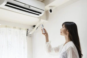 エアコンのスイッチを入れる女性の写真